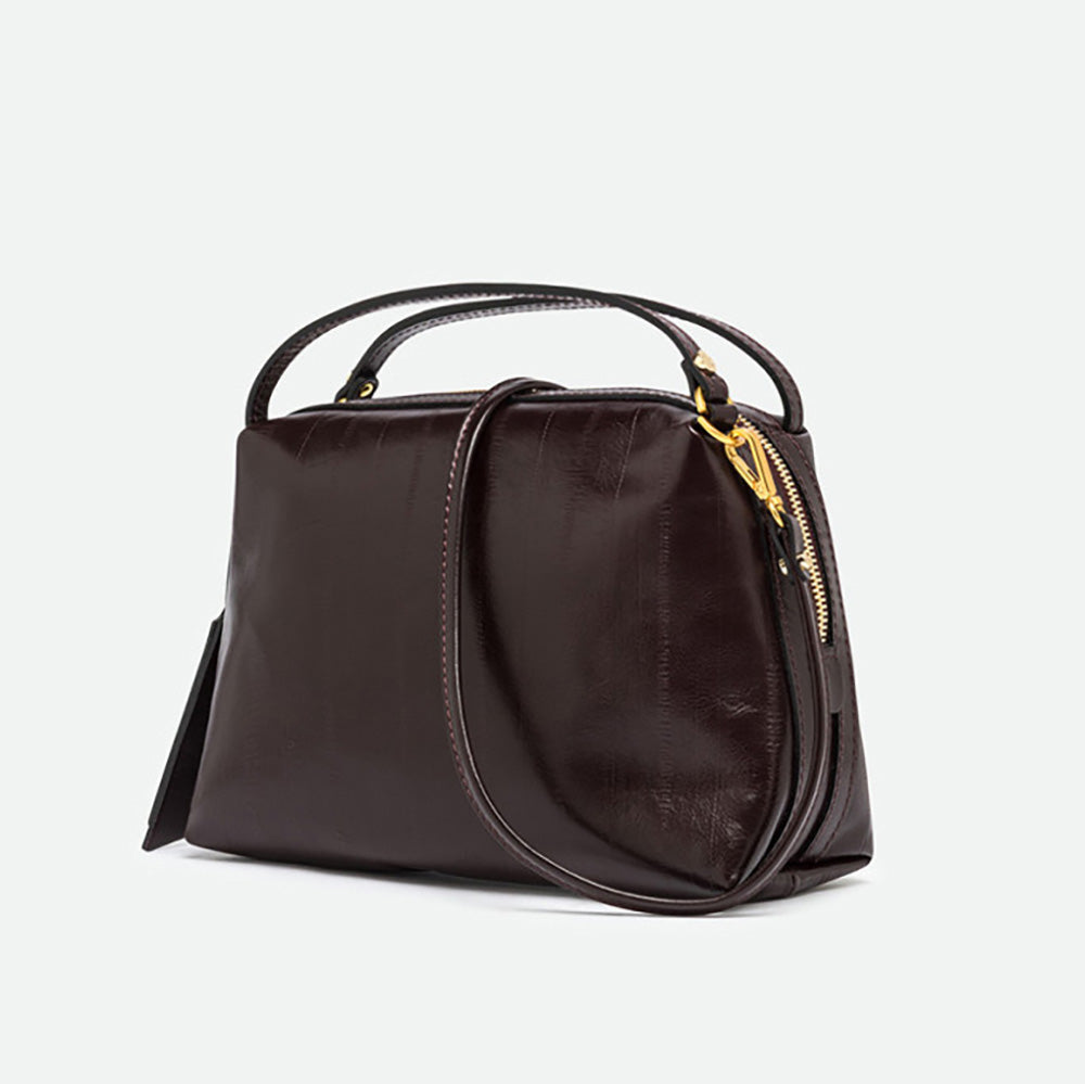 Angled view of a dark burgundy leather handbag with its long strap attached
