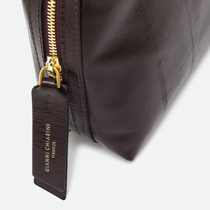 Close-up of a gold zip and leather pull tag on a glossy dark burgundy bag