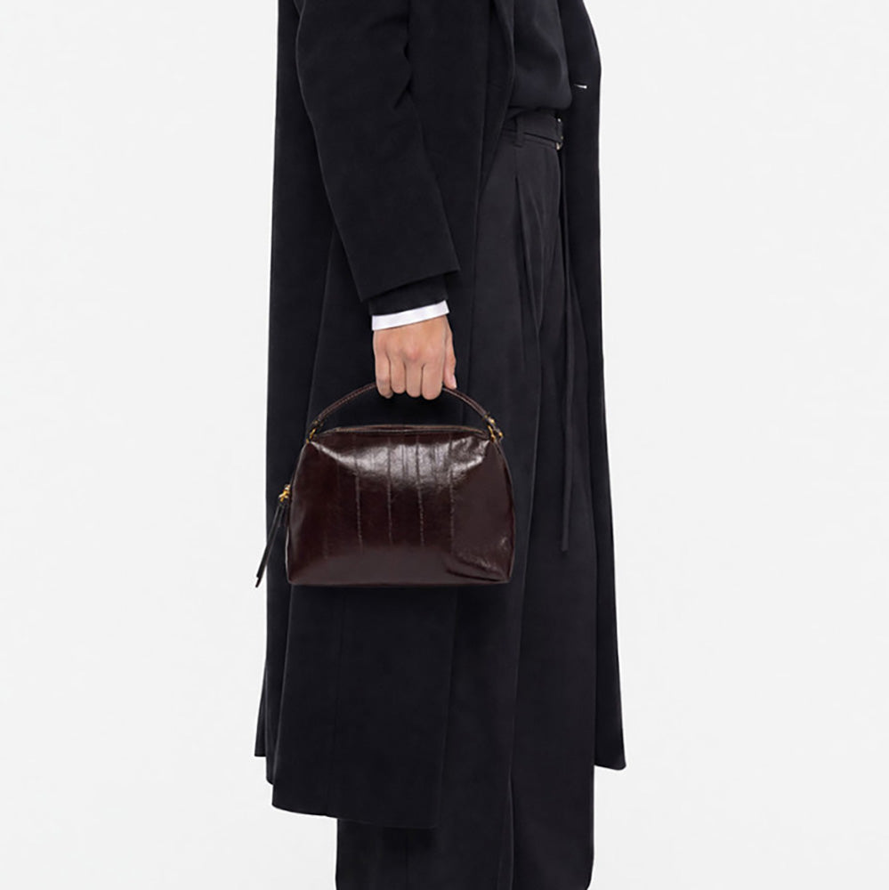 Woman in a black coat holding a small dark burgundy leather handbag by its handles