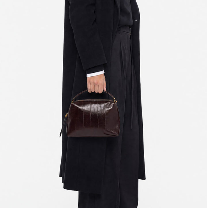 Woman in a black coat holding a small dark burgundy leather handbag by its handles