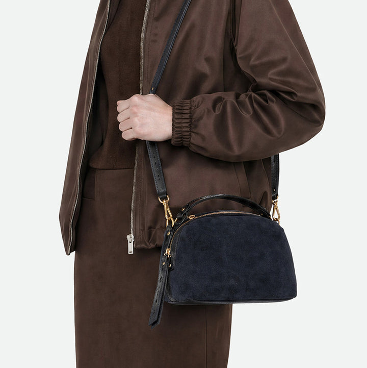 Woman in a brown jacket wearing a small navy suede bag across the body