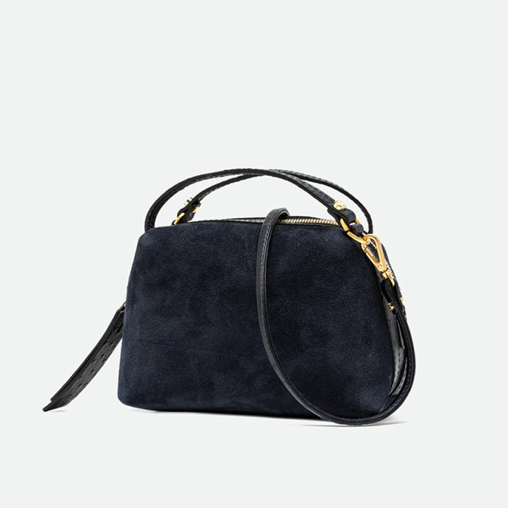 Angled view of a navy suede handbag with gold clasps and its crossbody strap