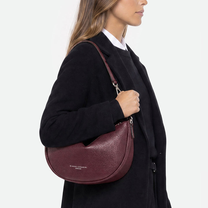 Woman in a black coat wearing a burgundy half moon bag on her shoulder