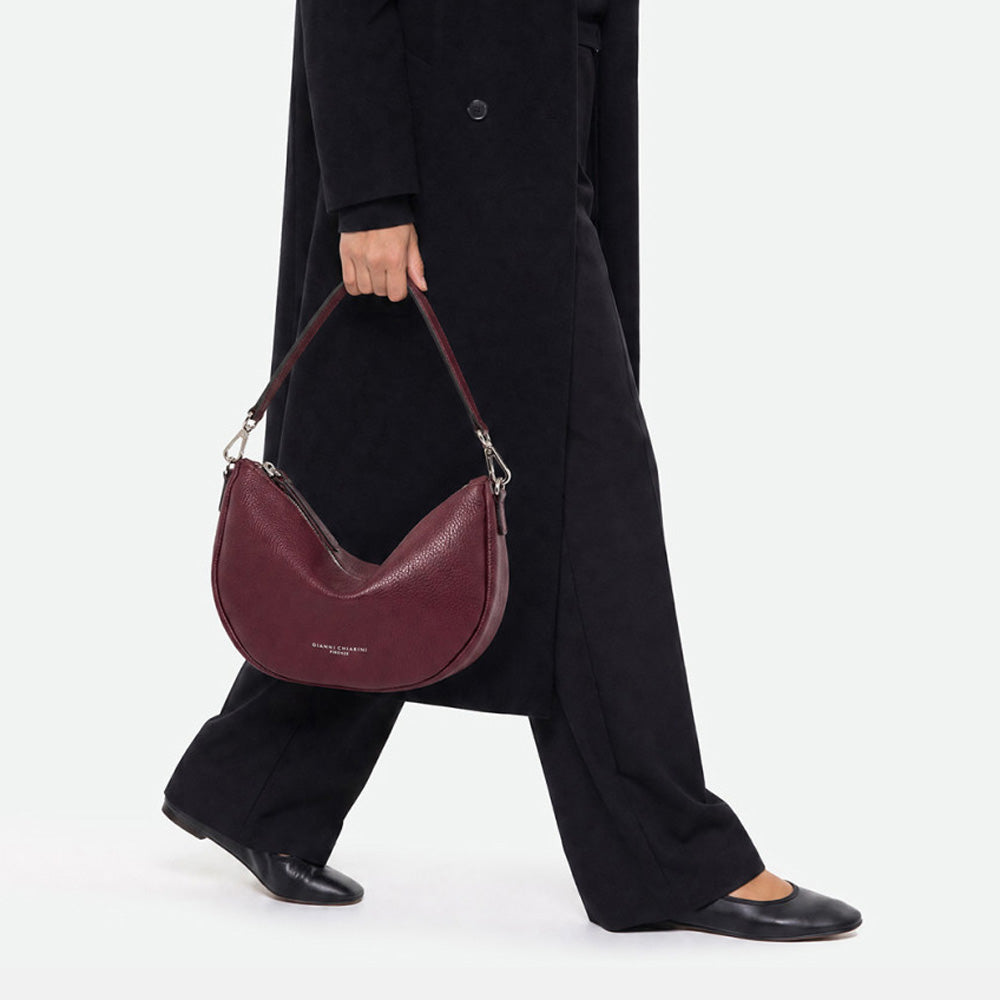 Woman walking with a burgundy half moon bag held by its shoulder strap