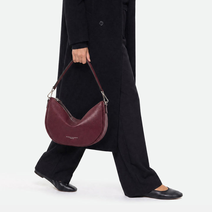 Woman walking with a burgundy half moon bag held by its shoulder strap
