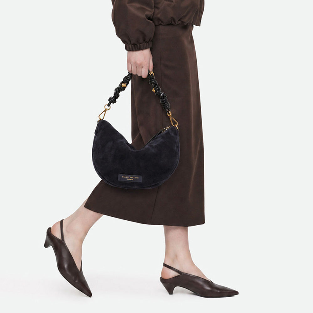 Woman in a brown skirt carrying a navy suede half moon bag by its ruched handle