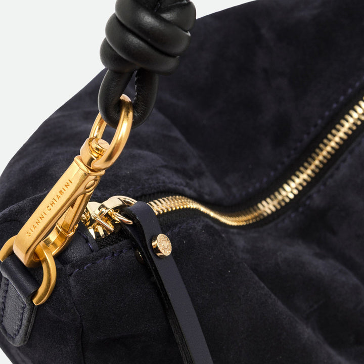 Close-up of a gold clasp and ruched black leather handle on navy suede