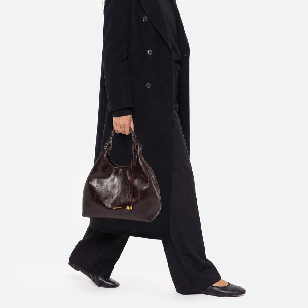 Woman in black carrying a glossy dark burgundy tote bag by its handles