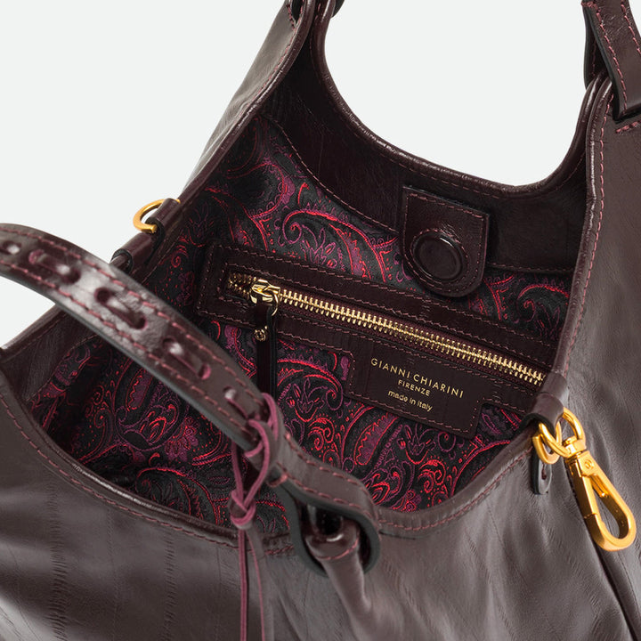 Inside a dark burgundy tote showing a red and purple paisley lining and gold zip pocket