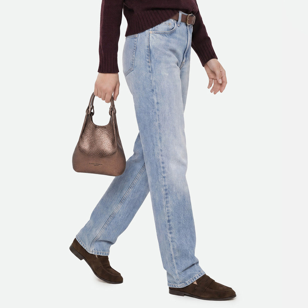 Woman in jeans carrying a small bronze metallic bag by its handles