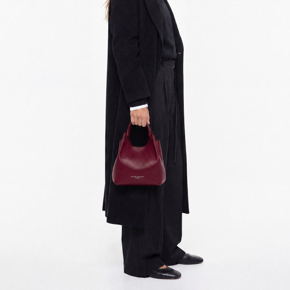 Woman in a long black coat holding a small deep red leather bag