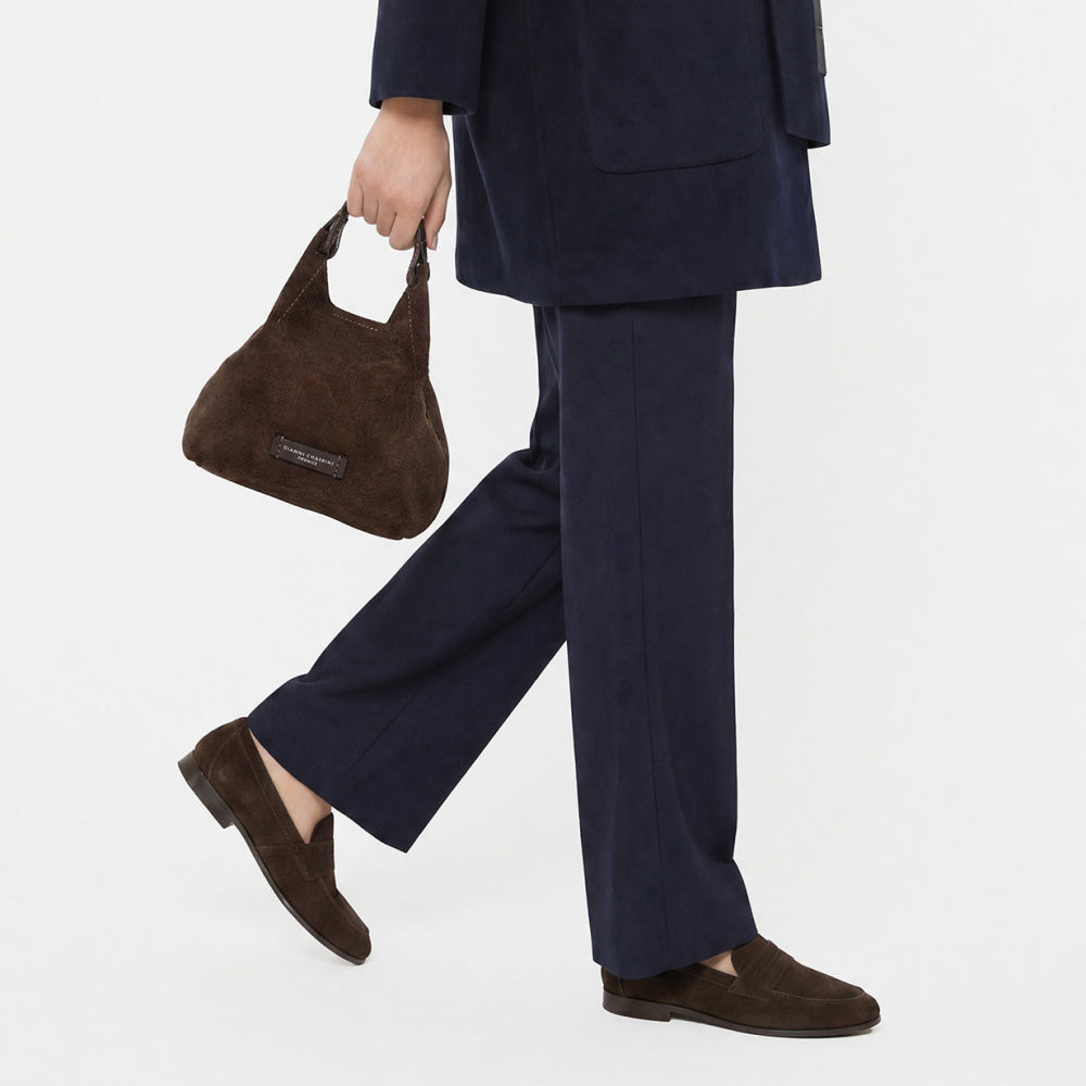 Woman in navy trousers carrying a small dark brown suede bag by its handles