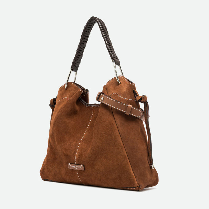 Angled view of a tan suede shoulder bag with a braided handle and silver rings