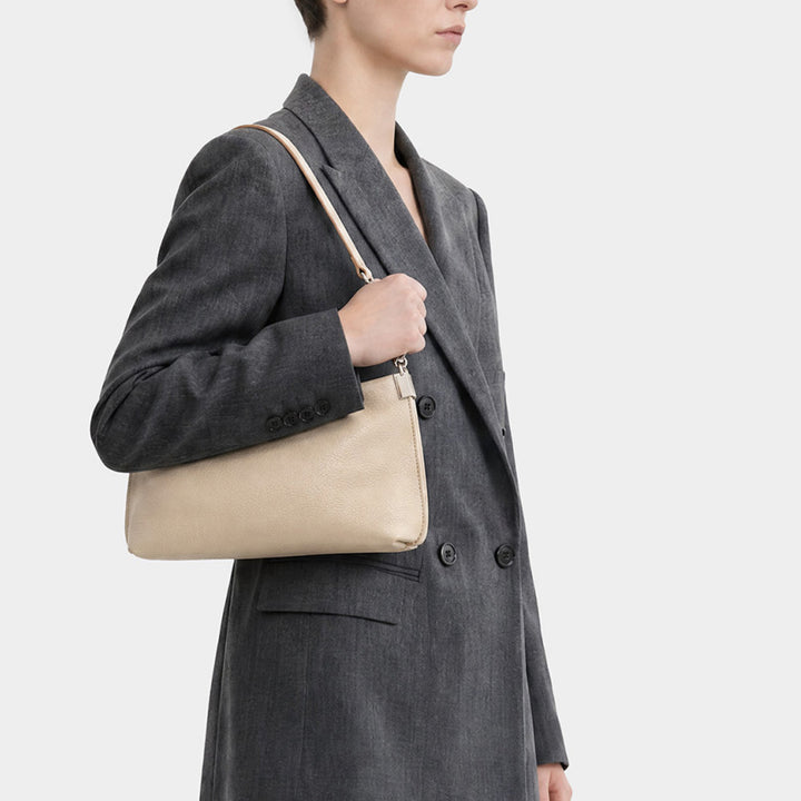 Woman in a grey blazer wearing a slim cream leather bag on her shoulder