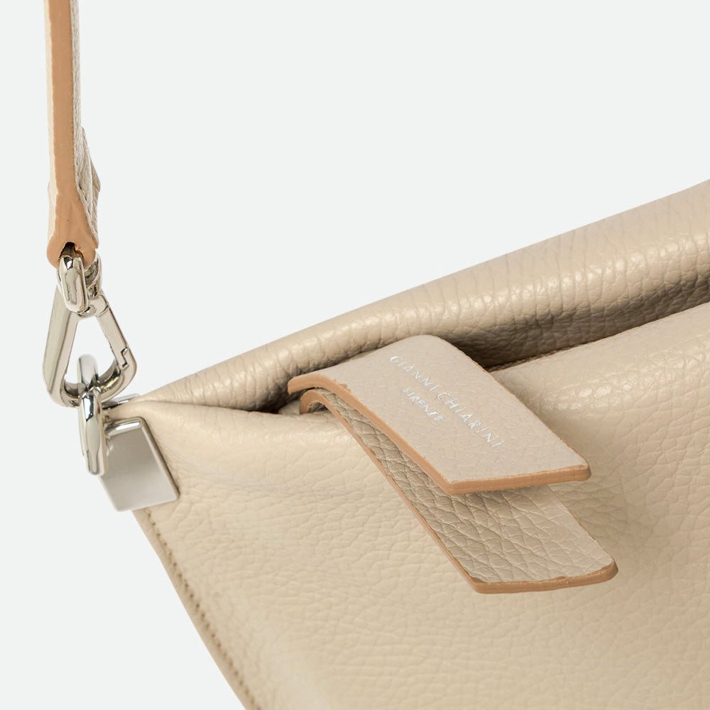 Close-up of a silver clasp and leather strap tab on a cream leather bag