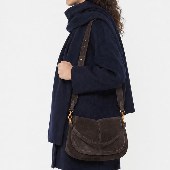 Woman in a navy coat wearing a dark brown suede saddle bag on her shoulder