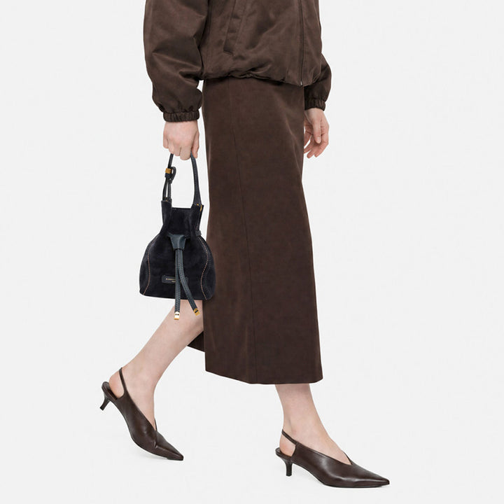 Woman in a brown skirt carrying a small navy suede bucket bag