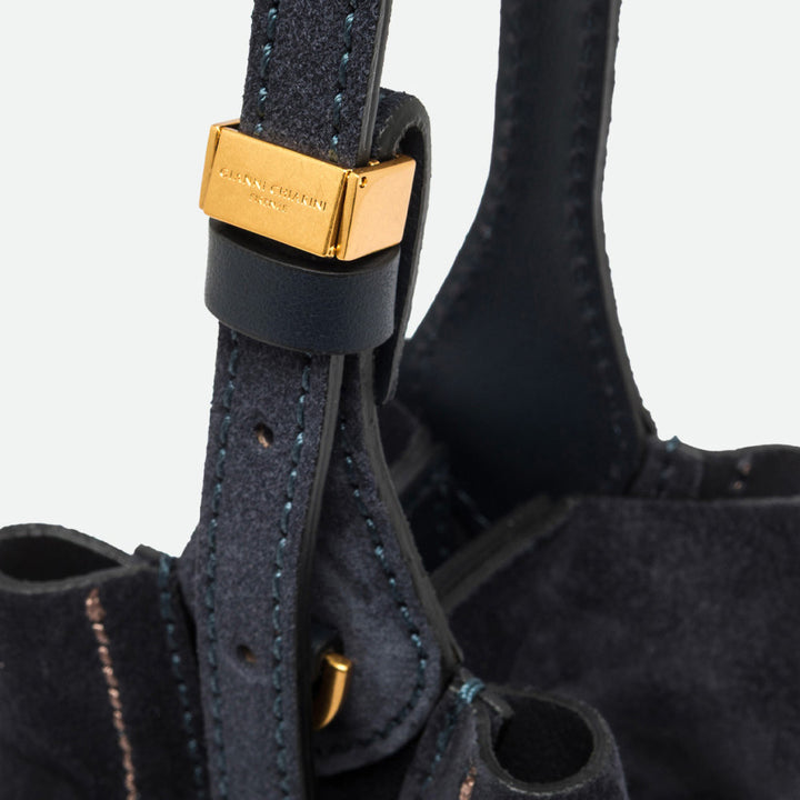 Close-up of a gold buckle on the navy leather strap of a suede bucket bag