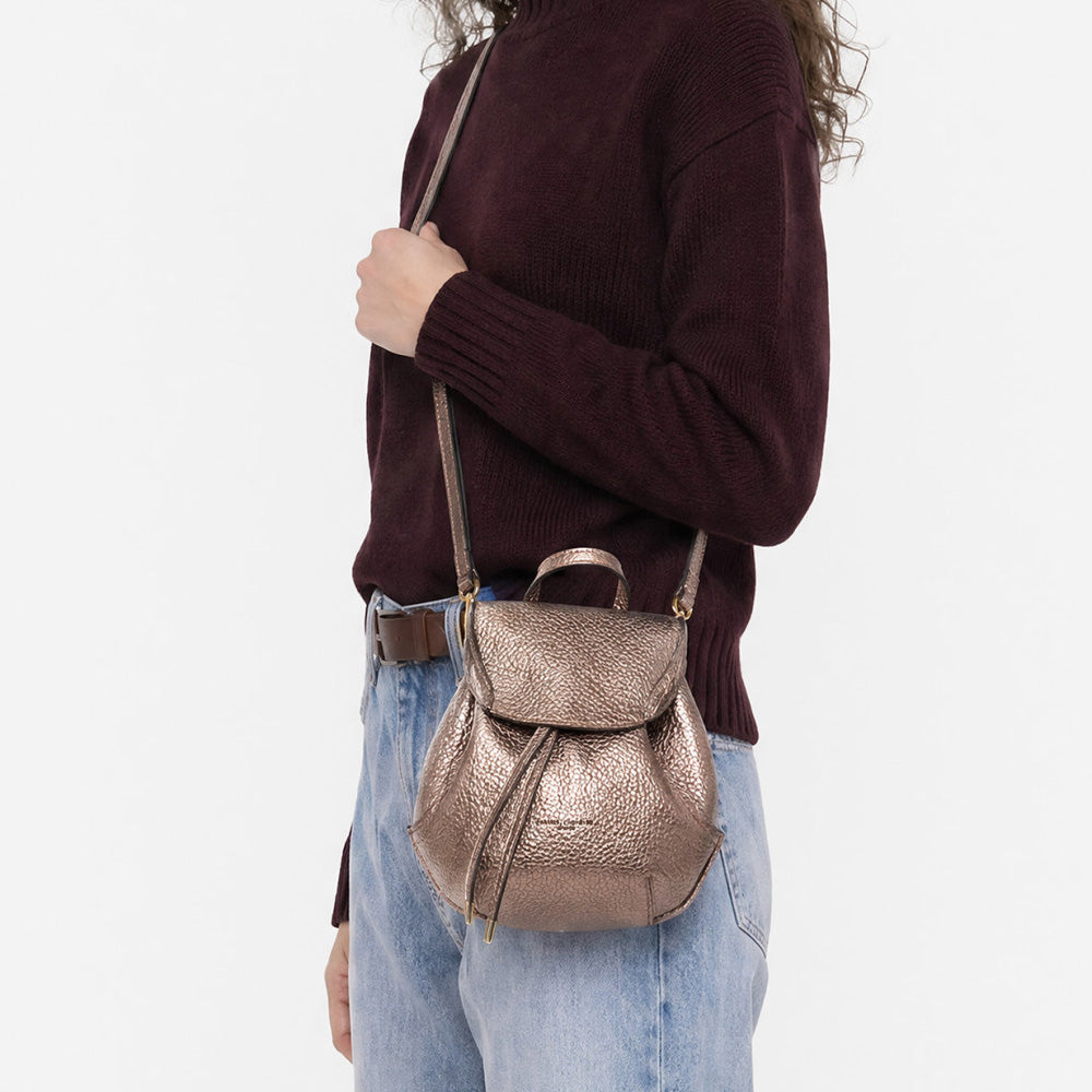 Woman in jeans and a burgundy jumper wearing a small bronze metallic backpack on one shoulder