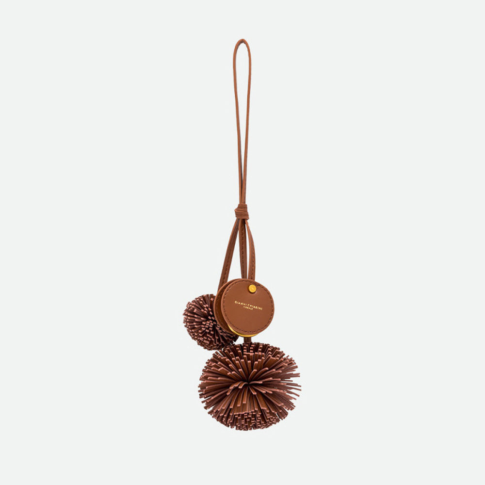 Brown bag charm with two fringed pompoms, a round branded disc and a long loop