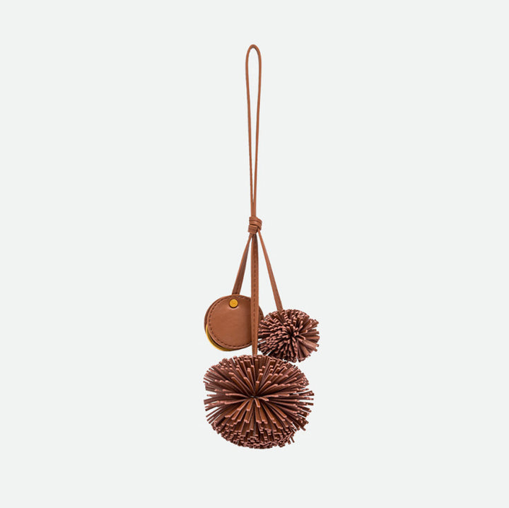 Reverse side of a brown pompom bag charm with a round disc