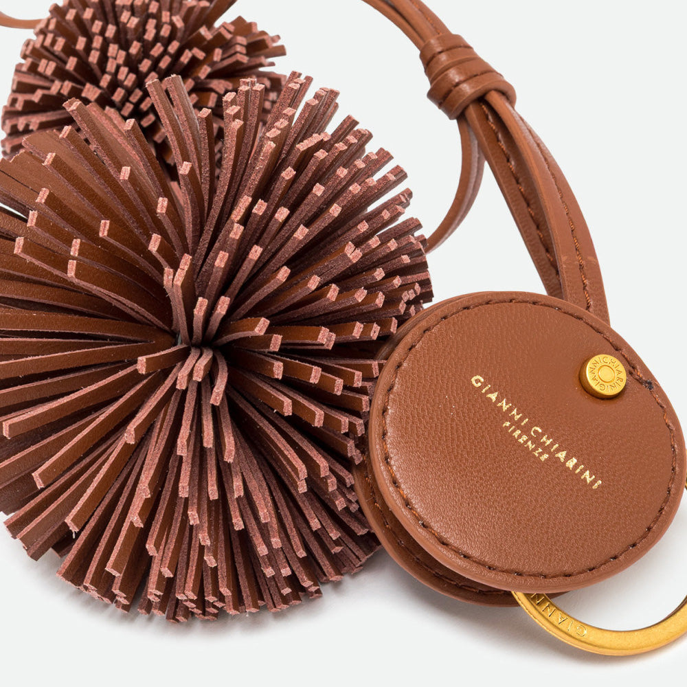 Close-up of a fringed brown pompom and round branded disc with a gold stud