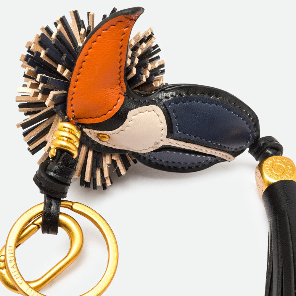 Close-up of a toucan bag charm showing its orange beak, fringed crest and gold clasp