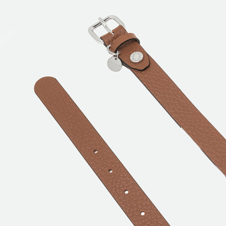 Close-up of a tan leather belt showing the silver buckle, charm and punched holes