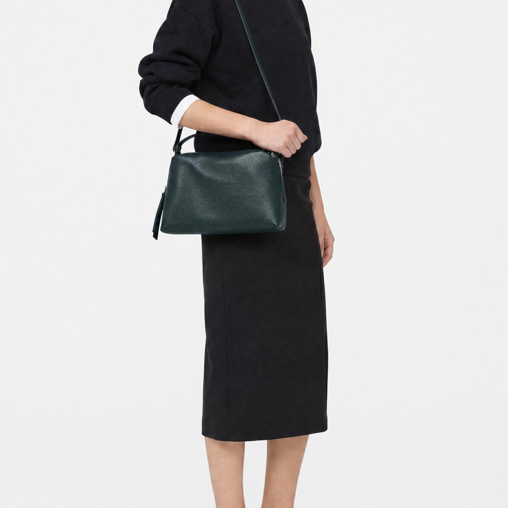 Woman in a black skirt wearing a dark green leather bag across the body