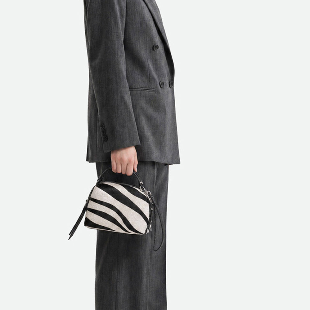 Woman in grey trousers holding a small zebra print handbag