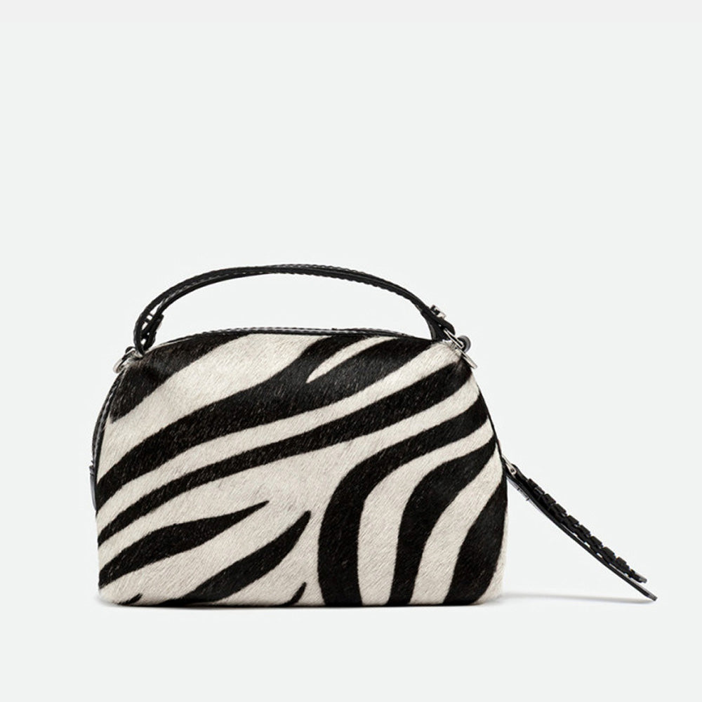 Front of a small zebra print handbag with a zip top and black leather handles
