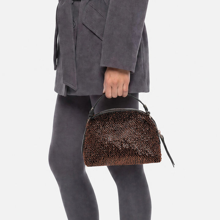 Woman in grey holding a small bronze sequinned handbag by its handles