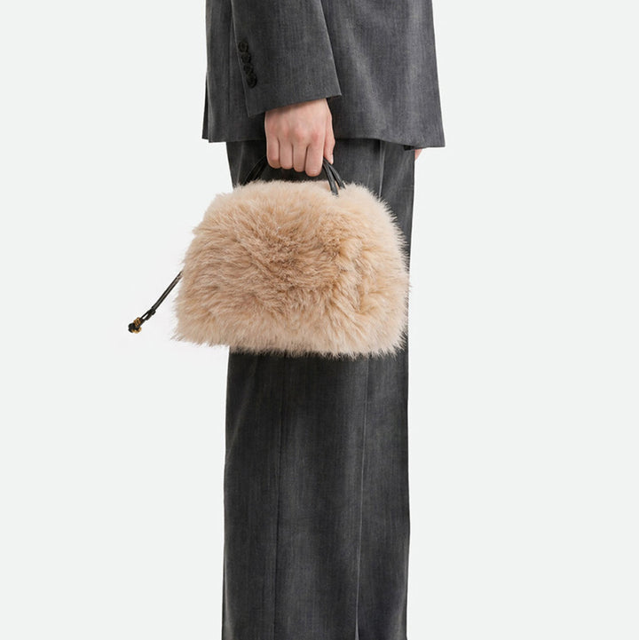 Woman in grey trousers holding a small cream faux fur handbag