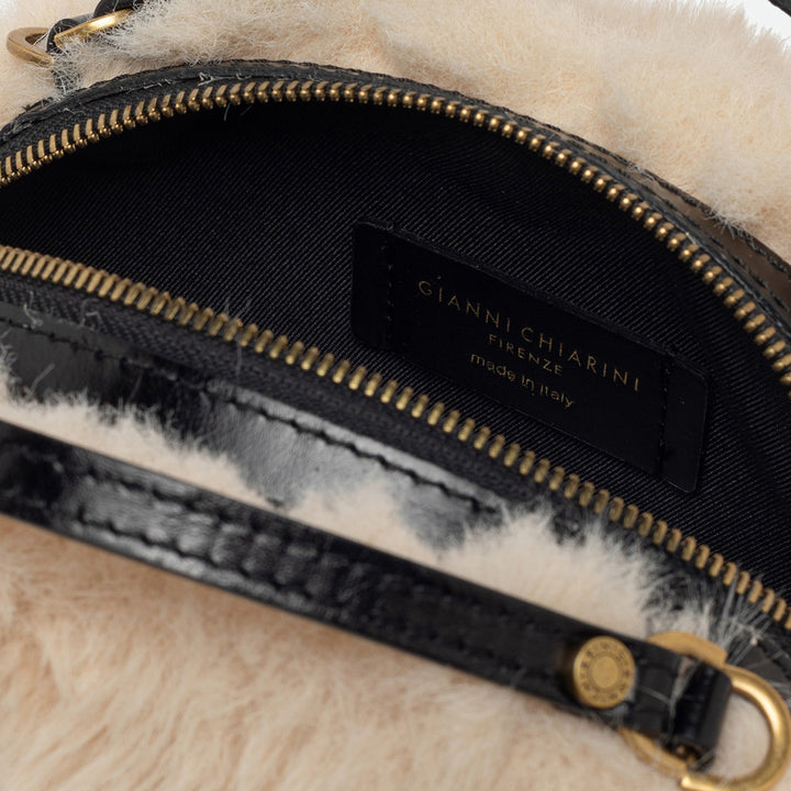 Inside a cream faux fur bag showing a black lining and brass zip