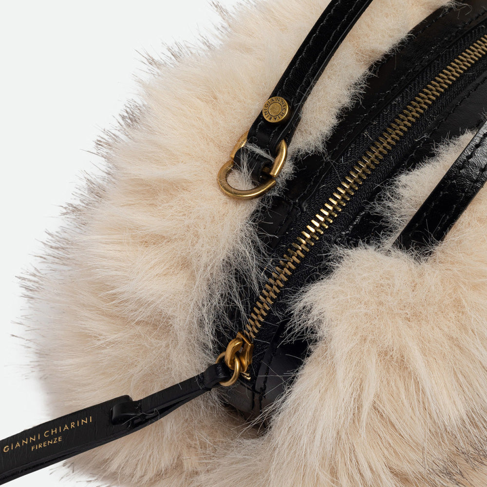 Close-up of fluffy cream faux fur with a brass zip and black leather trim