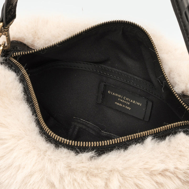 Inside a cream faux fur bag showing a black lining and brass zip