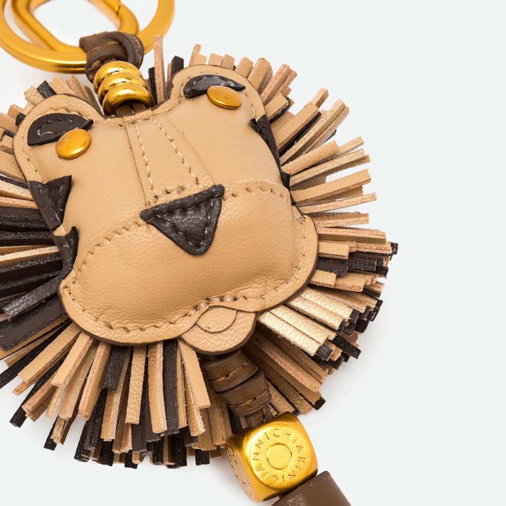 Close-up of a lion bag charm showing its face, fringed mane and gold bead