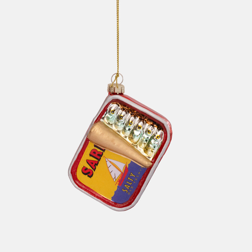 Glass ornament shaped like an open sardine tin with silver fish and a red, yellow and blue label, on a gold string