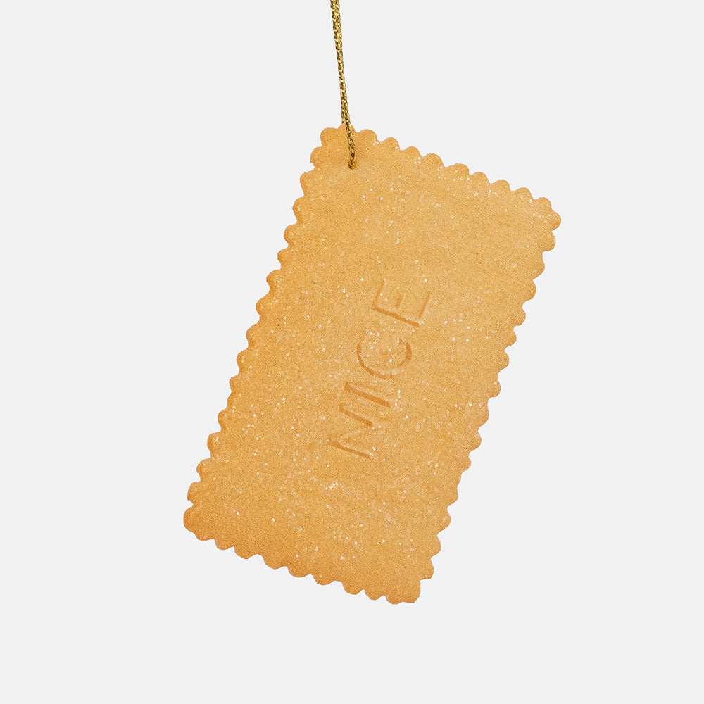 Reverse of a golden rectangular biscuit ornament with the word Nice pressed into its glittery surface