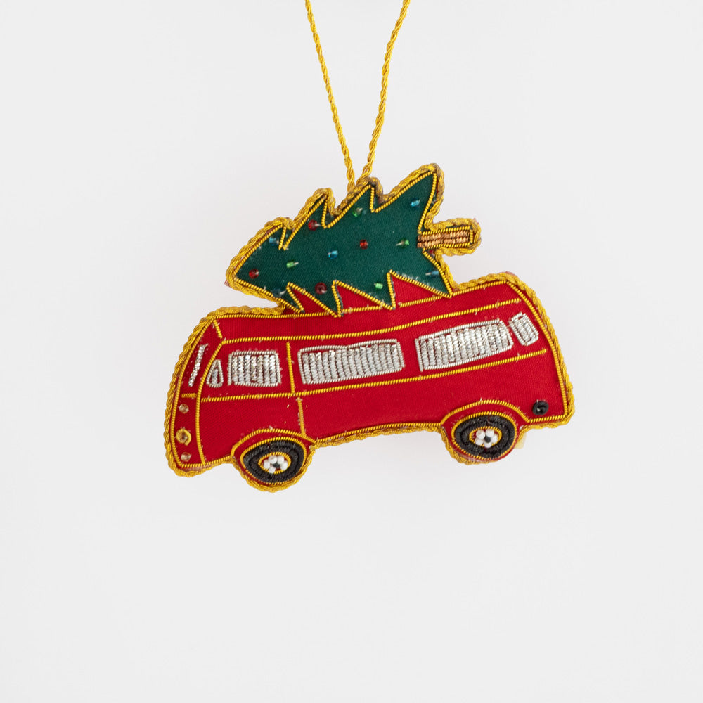 Beaded red bus Christmas tree decoration carrying a green fir tree on its roof, with gold embroidered details, hanging from a gold cord.