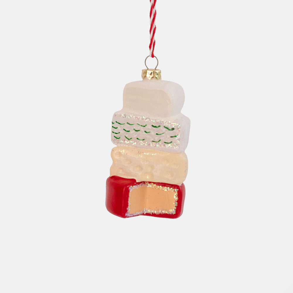 Glass ornament of four stacked cheeses in white, cream and yellow on a red waxed round, hung on a red and white string