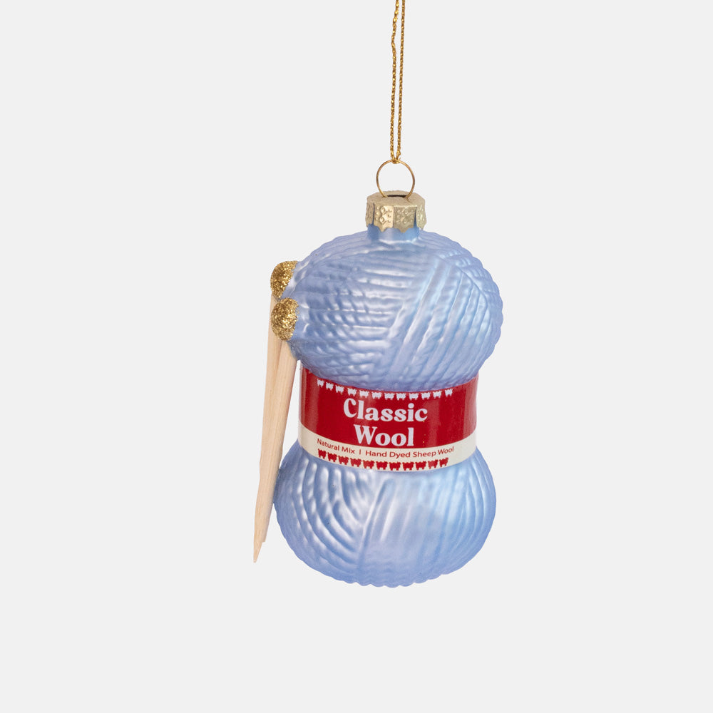Pale blue glass ornament shaped like a skein of wool with a red label and two wooden knitting needles