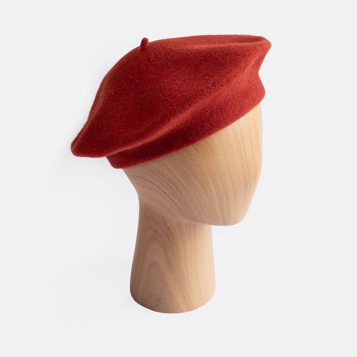 A classic dark orange felt beret displayed on a light wood mannequin head against a clean white background.