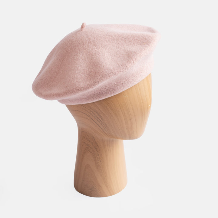 A dusty pink felt beret hat displayed on a light wood mannequin head against a clean white background.