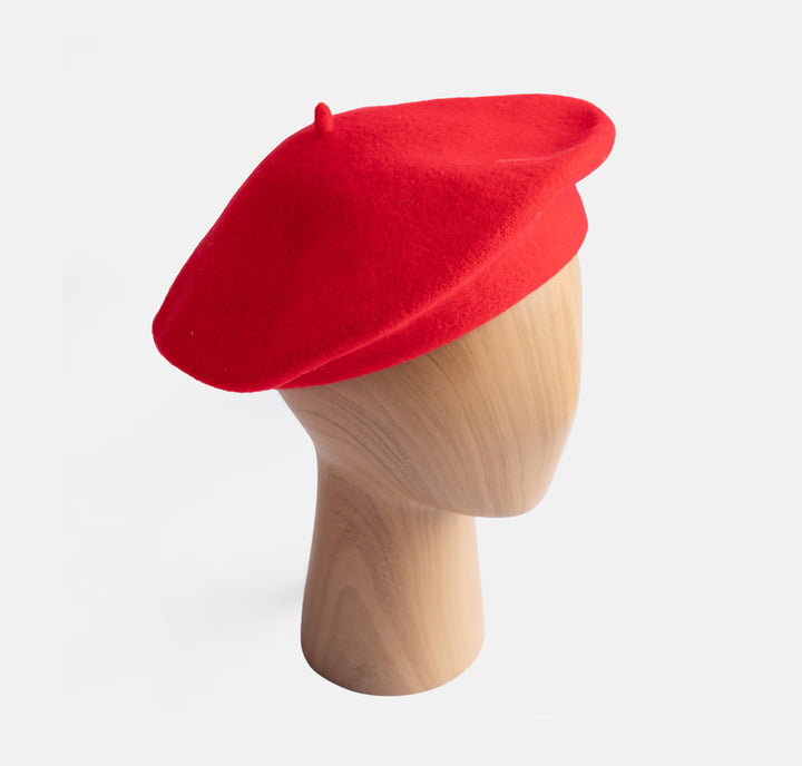 A bright red felt beret hat displayed on a light wood mannequin head against a clean white background.