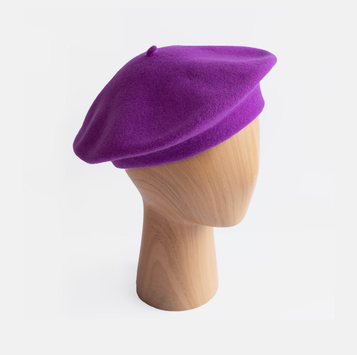 A purple wool beret hat displayed on a light wood mannequin head against a clean white background.