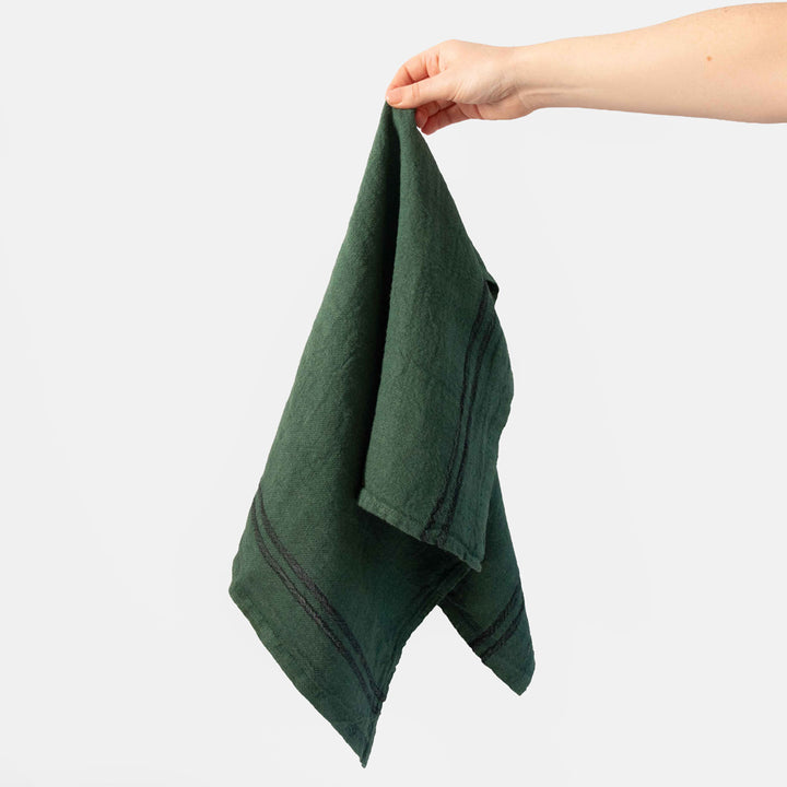hand holding a green tea towel with a dark stripe on a white background
