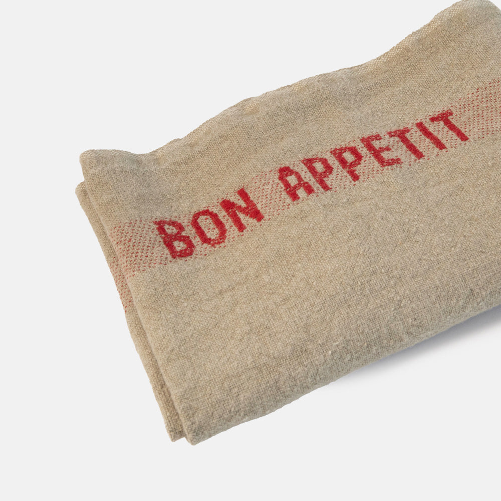 Beige tea towel with red 'Bon Appetit' text on a light grey background
