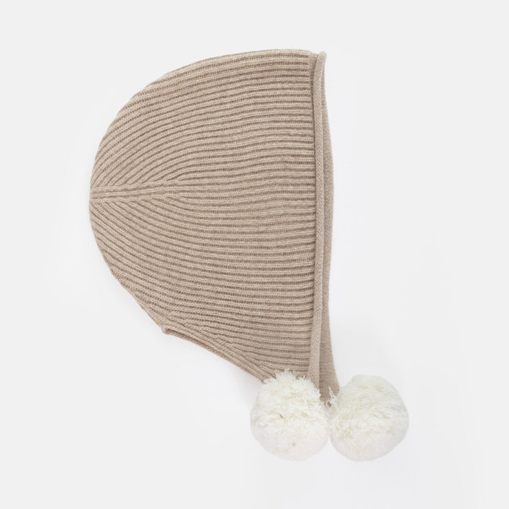 A beige ribbed knit bonnet hat with two fluffy white pom-poms, shown against a plain white background.