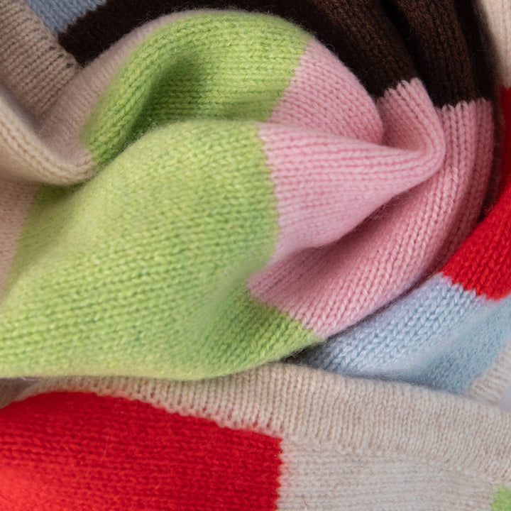 A close-up of a knitted fabric with large color-blocked sections in light green, pink, red, light blue, dark brown, and cream.